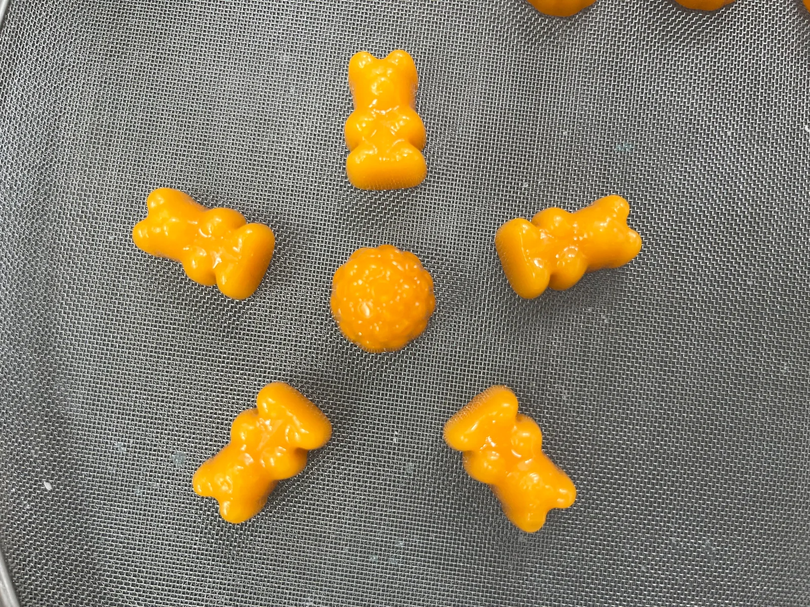 Orange bear-shaped and round gummy samples on a gray mesh surface, illustrating the shape checks used when screening creatine gummy samples for brand development.