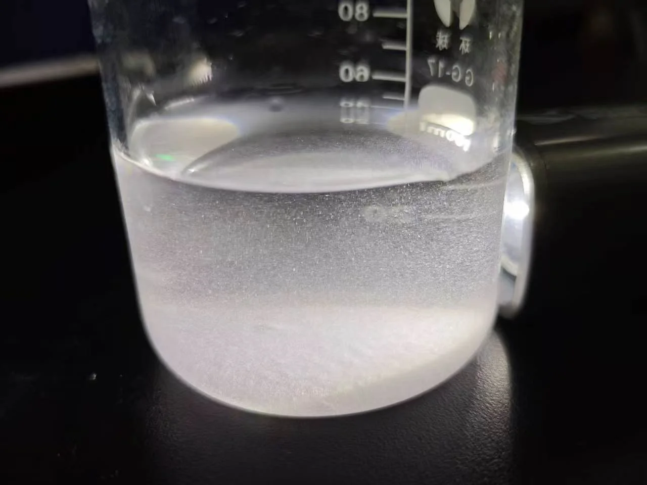 Beaker containing a cloudy liquid with white sediment at the bottom, illustrating the discussion of creatine monohydrate solubility during gummy sample screening.