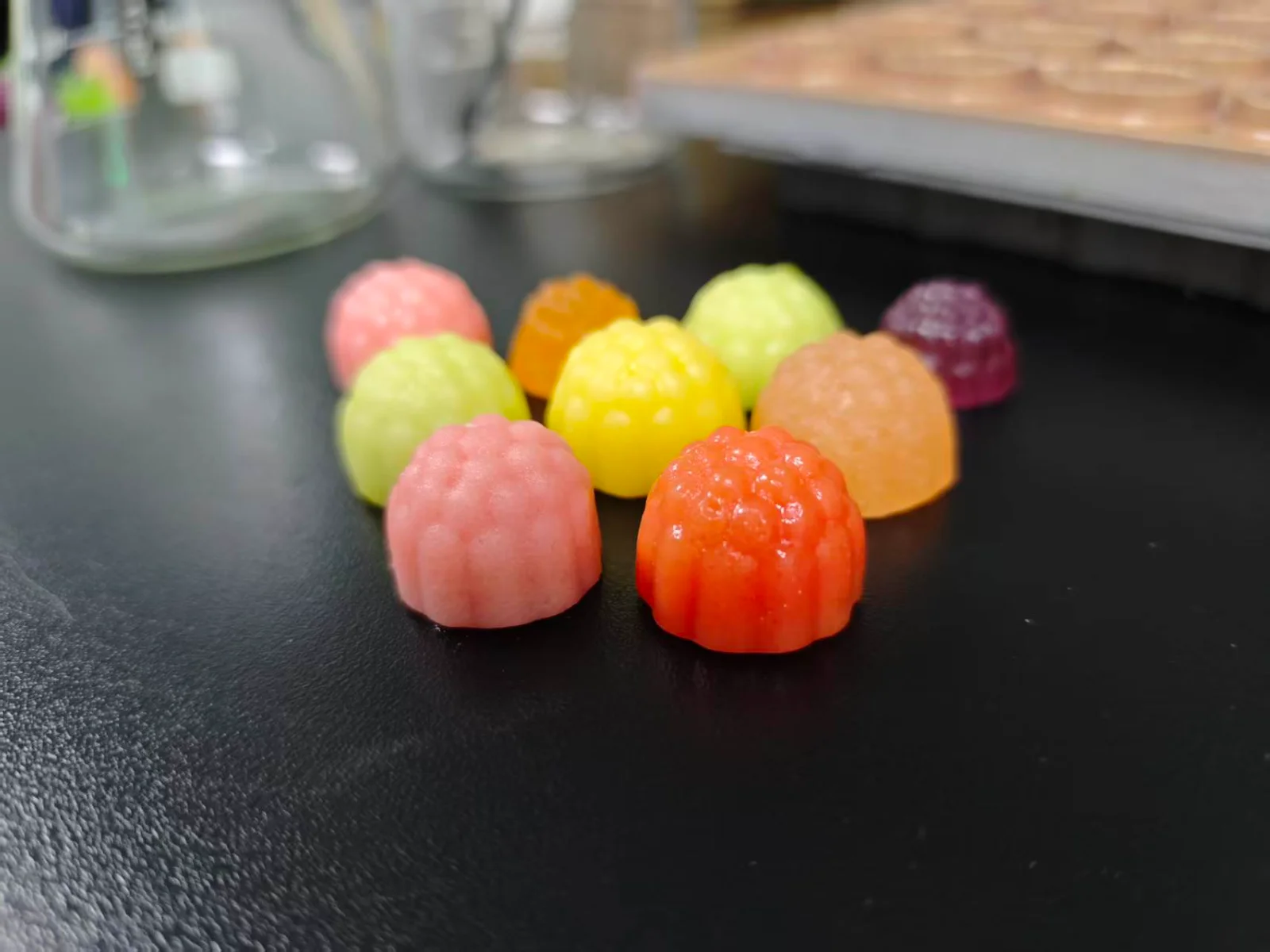 Colorful molded gummy samples arranged on a laboratory bench, illustrating flavor development options for creatine gummies, with glass containers in the background.