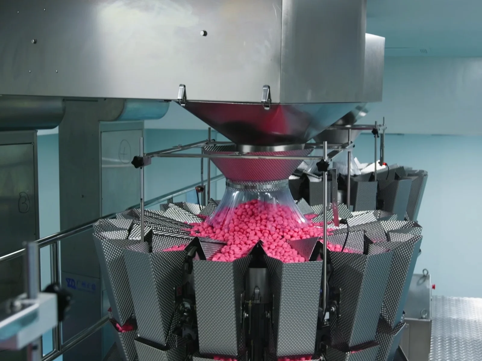 Pink gummies collected in a stainless steel multihead weighing machine, illustrating the manufacturing context for comparing creatine gummy and powder product development.