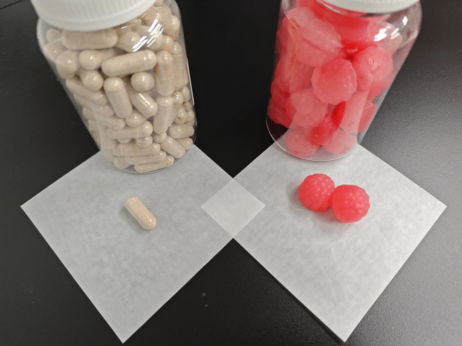 Clear bottles of beige capsules and red berry-shaped gummies, illustrating the format comparison for magnesium glycinate supplement product development.