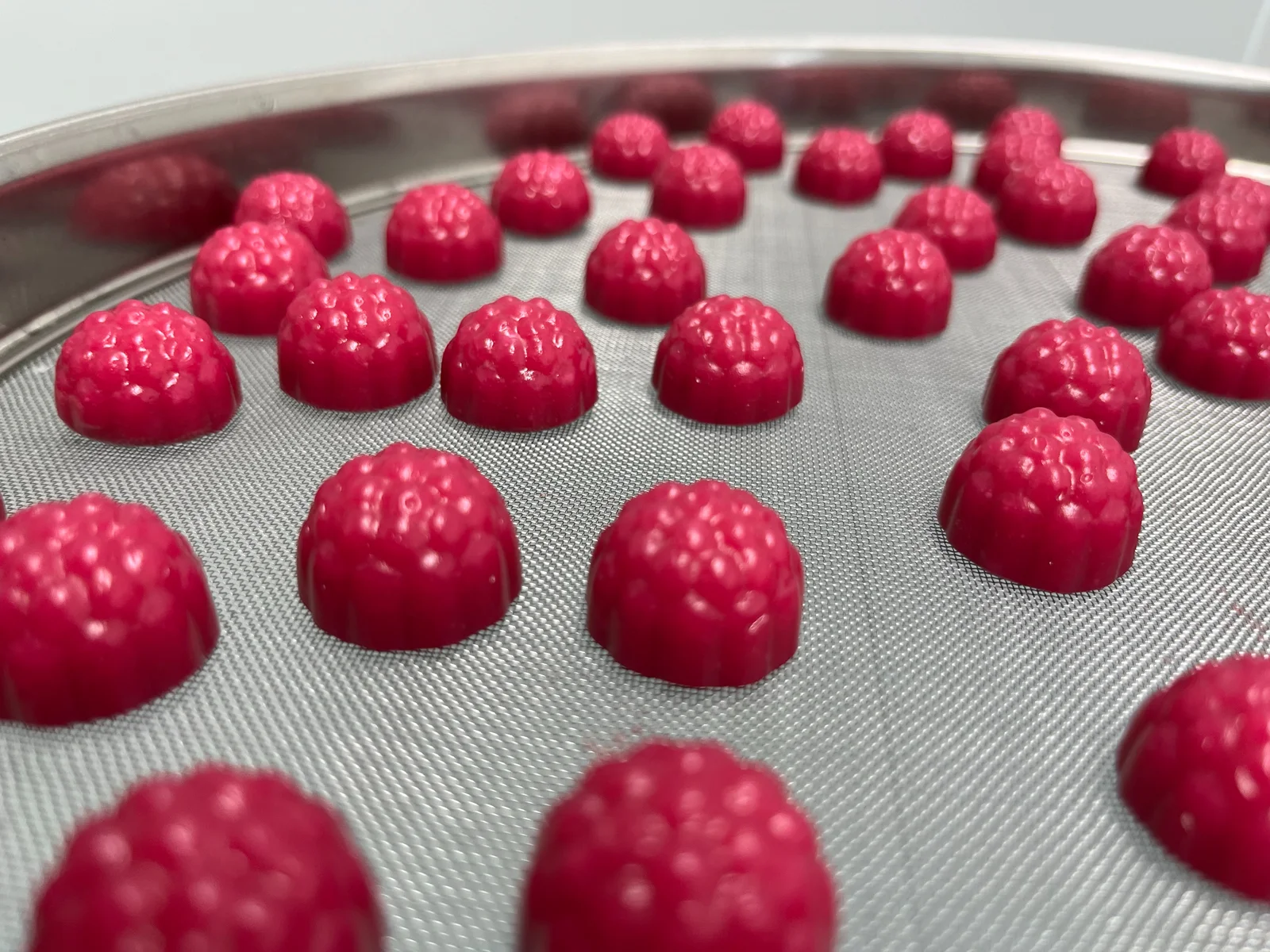 Red berry-shaped gummies arranged across a round mesh tray, accompanying magnesium glycinate gummy formulation ideas discussed in the article's section on menstrual support.