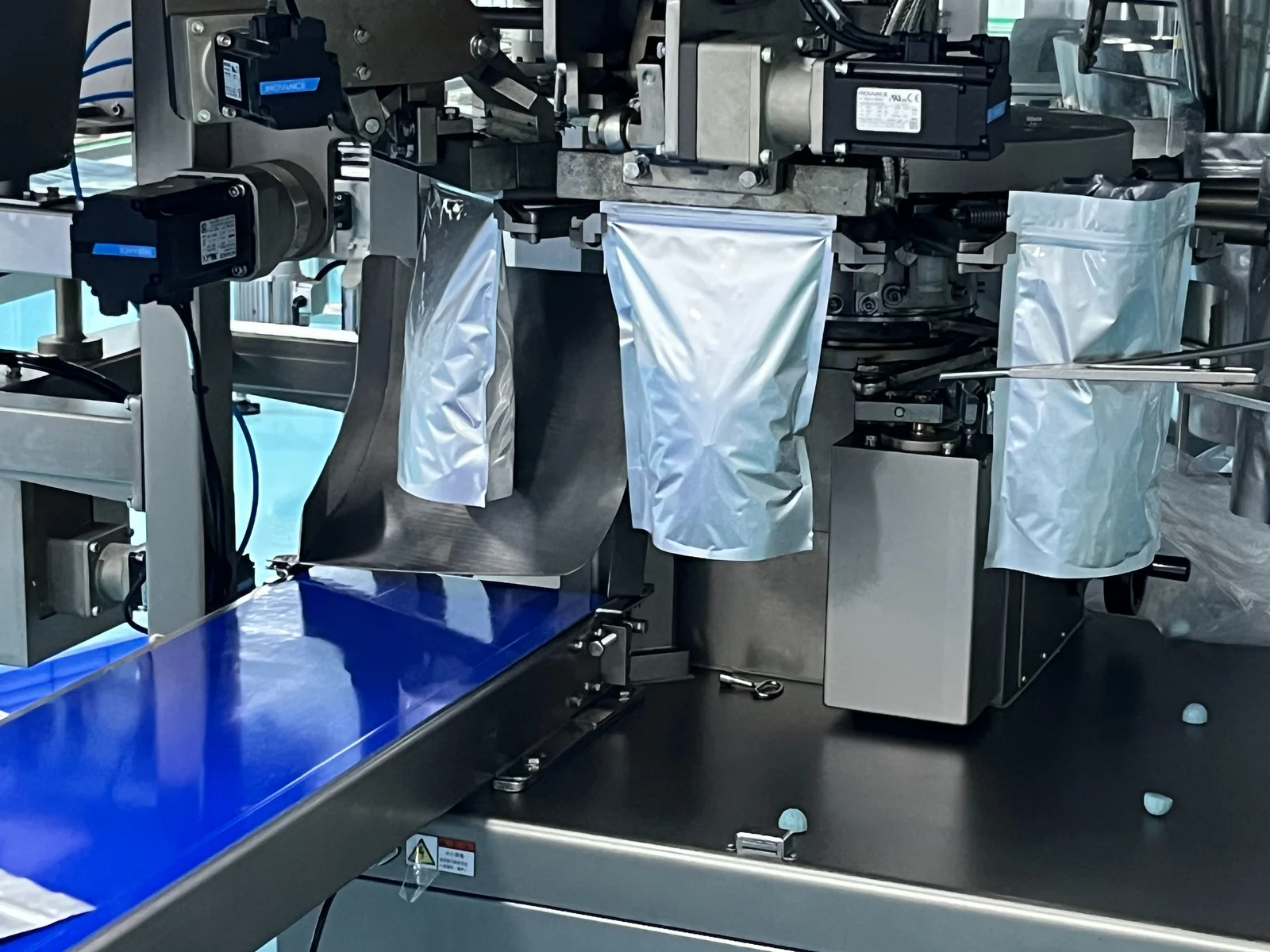 White pouches positioned on automated packaging equipment beside a blue conveyor, illustrating packaging considerations within magnesium glycinate gummy product development for supplement brands.