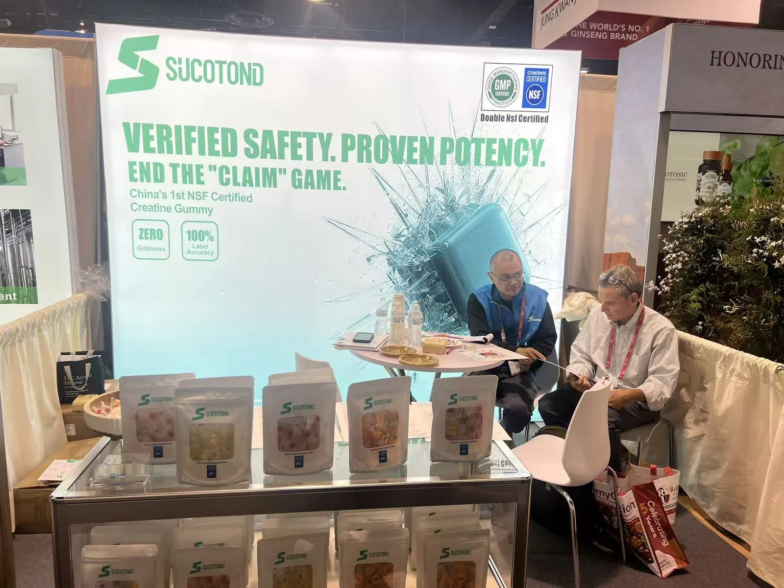 Two people seated at the SUCOTOND booth discussion table with packaged gummies in front