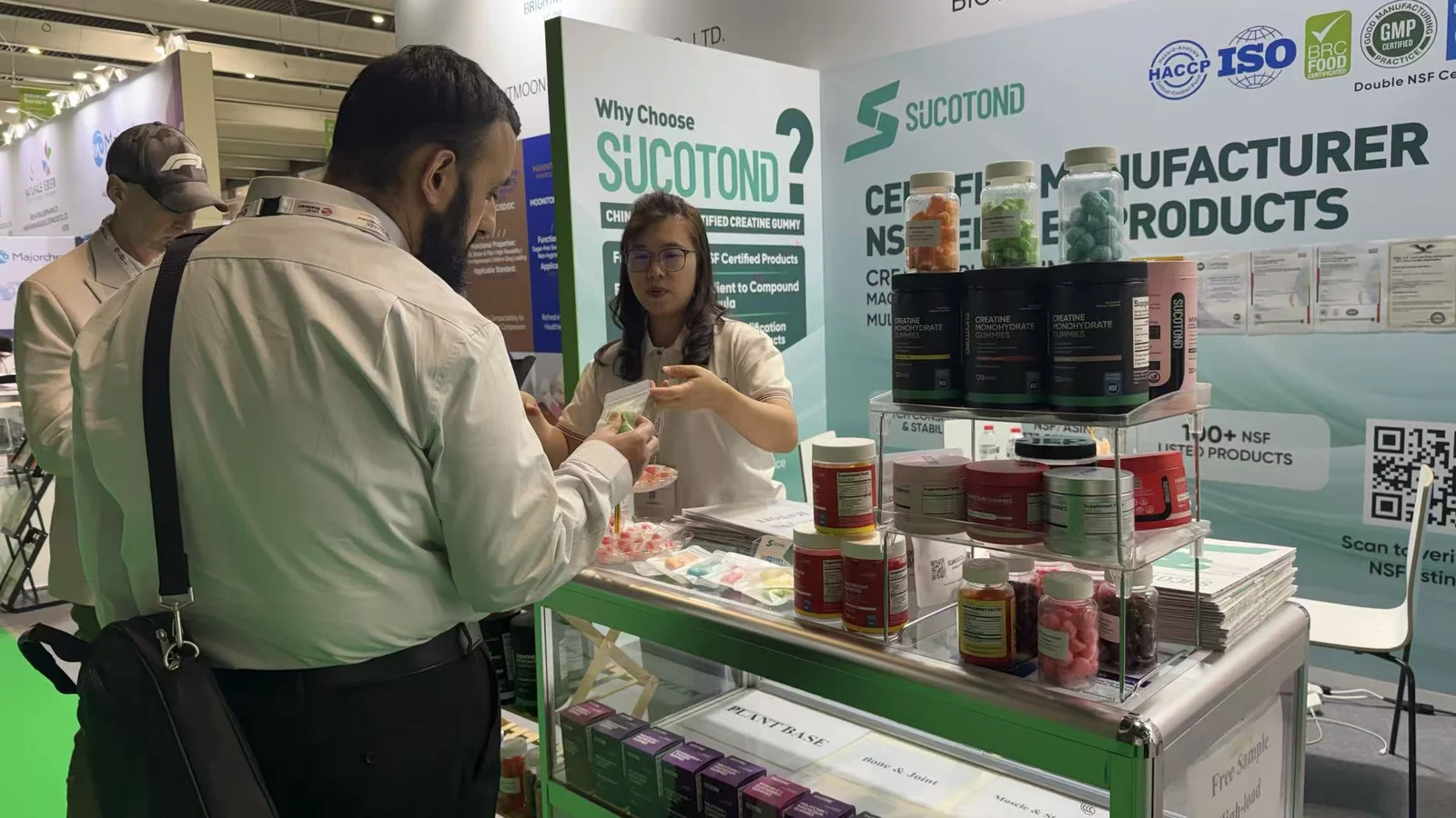 A visitor speaks with a SUCOTOND representative beside shelves of gummy products