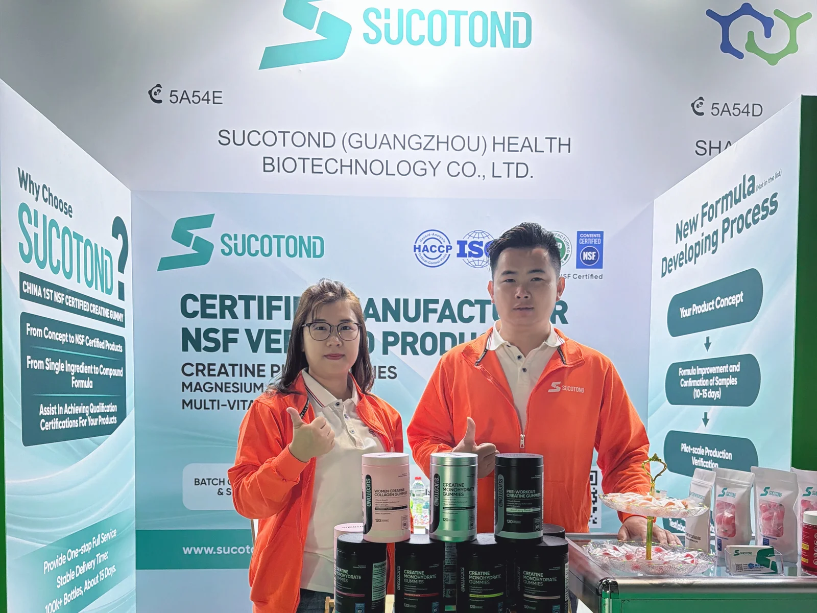 Two SUCOTOND team members in orange jackets pose behind the gummy display at stand 5A54E