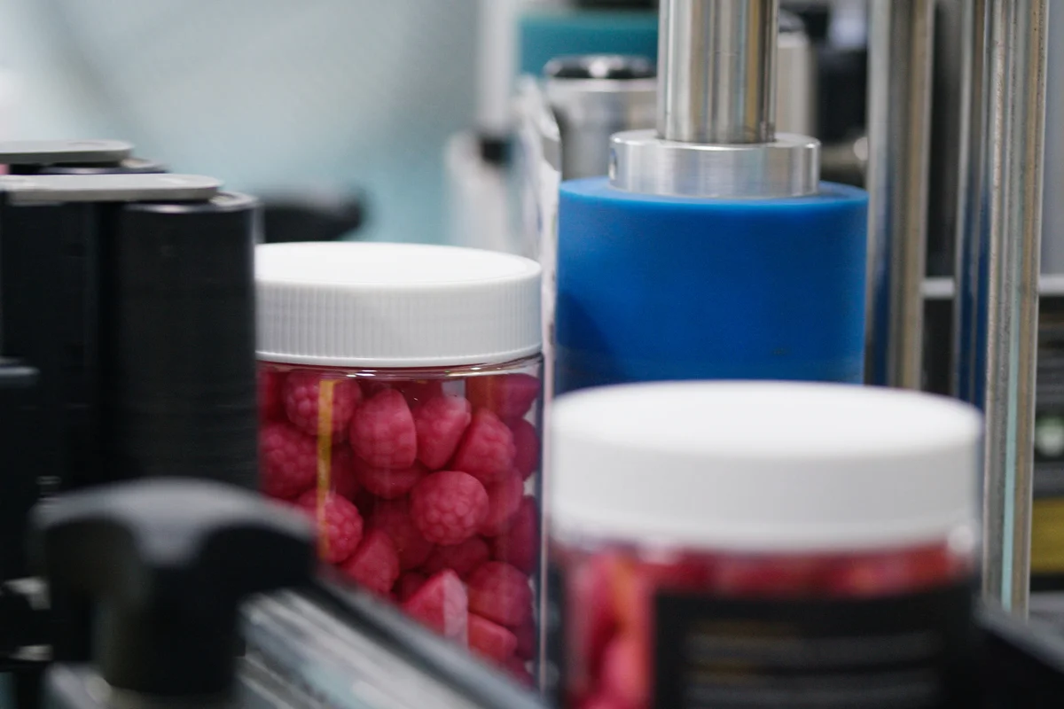 Clear bottles filled with pink gummies on a packaging line