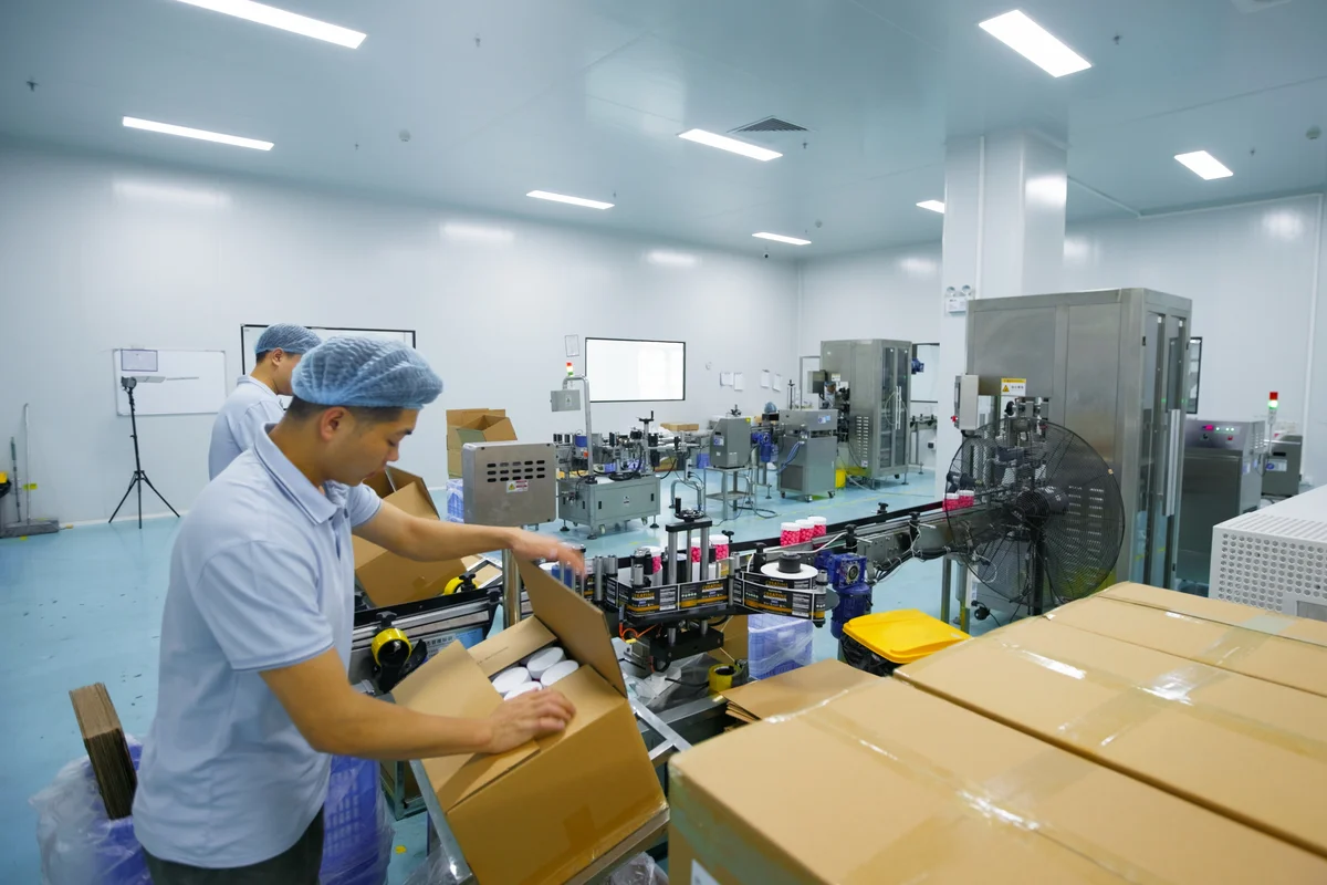 A worker packs gummy bottles into a shipping carton beside the bottling line