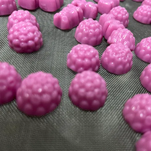 Purple textured gummy samples on a mesh tray for chew and surface review