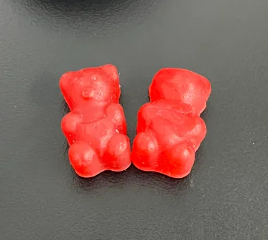 Two red bear shaped gummy samples displayed alone on a dark surface for a sugar free BCAA gummy concept