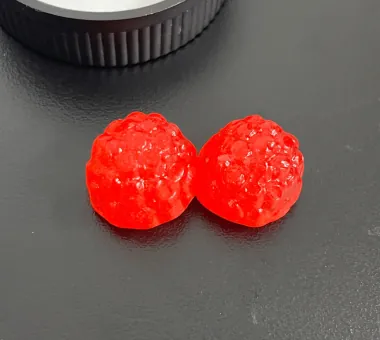 Two bright red textured gummy samples on a dark tabletop for a Nitric Oxide Beet Root Gummies product concept