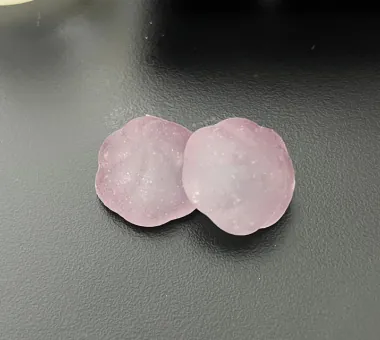 Two pale pink round gummy samples on a dark tabletop for a Sugar-Free Beetroot Gummies concept