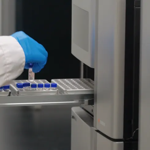 Gloved laboratory technician placing samples into analytical equipment for quality control of greater-than-99% creatine purity and fermentation-derived all-trans vitamin K2 MK-7 raw materials.