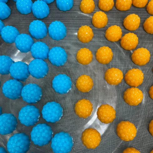 Blue and orange berry-shaped gummy samples in separate groups on a sieve