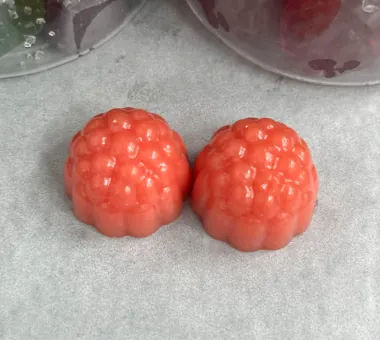 Two coral berry-shaped gummy samples on pale parchment