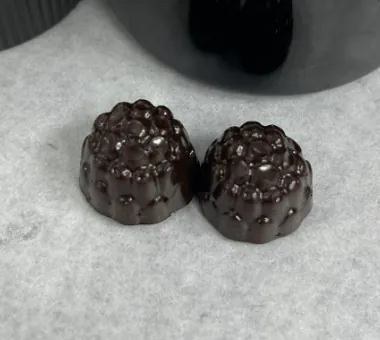 Two dark berry-shaped gummy samples displayed on pale parchment