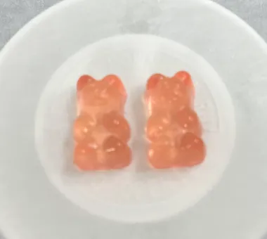 Two peach-colored bear-shaped gummy samples displayed in a white dish