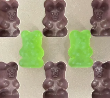 Two green bear-shaped gummy samples among purple gummy bears on a white display card