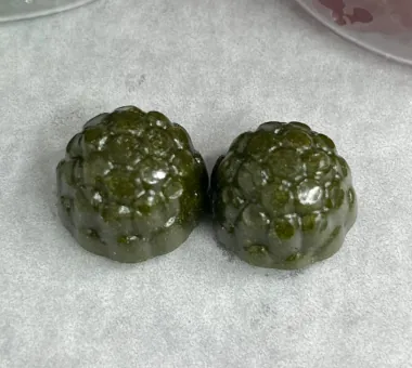 Two olive green berry-shaped gummy samples on pale parchment