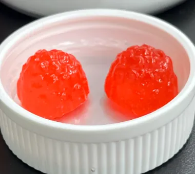 Two red berry-shaped gummy samples displayed in a white ramekin