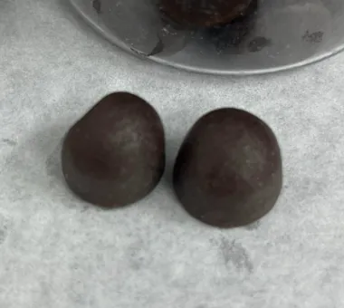 Two dark dome-shaped gummy samples on pale parchment