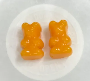Two orange bear-shaped gummy samples in a white dish