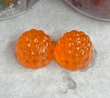 Two orange berry-shaped gummy samples on parchment
