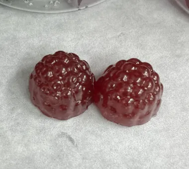 Two dark burgundy berry-shaped gummy samples on parchment