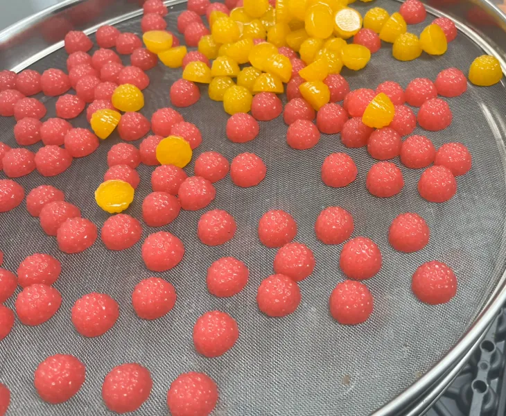 Red and yellow berry-shaped magnesium gummies on a production screen, showing natural flavor options developed to mask metallic and mineral notes in magnesium gummy formulations.