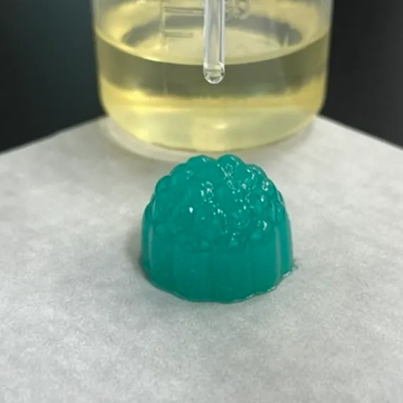 Green mushroom gummy sample beside a beaker and dropper, representing mixed berry flavor masking, moisture control and surface hardening options for chewy custom mushroom gummies.