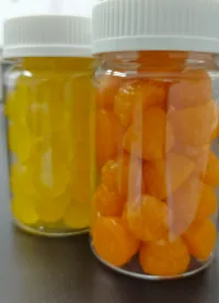 Bottled yellow and orange gummy samples for a men's protein CoQ10 gummies project, using emulsifier systems to keep fat-soluble CoQ10 uniformly dispersed in the protein mixture.