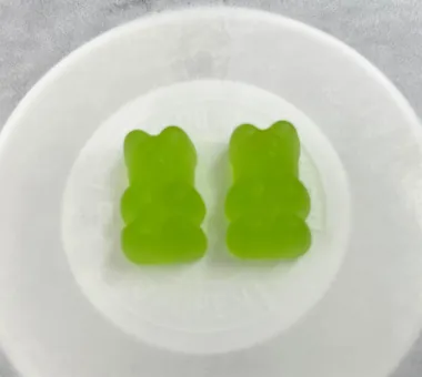 Two green bear-shaped gummy samples in a white dish for the Natural Shilajit Gummies product concept