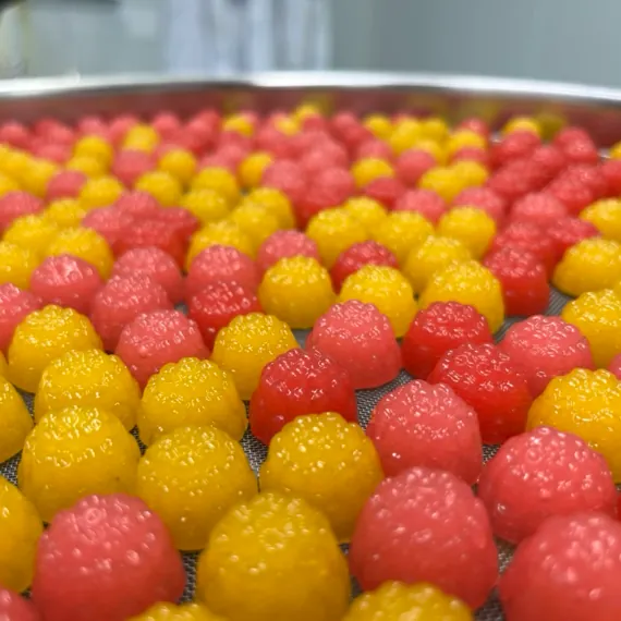 Red and yellow berry-shaped vitamin gummies on a production screen, showing color and flavor options used to balance texture, acidity, taste and appearance in custom Vitamin C and B-vitamin gummy formulas.