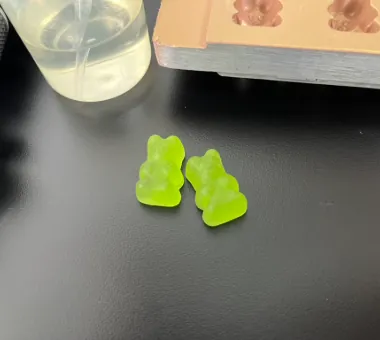 Two bright green bear-shaped collagen Vitamin C gummies representing a specialized premium formula made with collagen ingredients selected to avoid a fishy taste for skin-support product positioning.