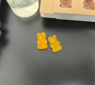 Two yellow bear-shaped high-potency Vitamin C gummies beside a sample beaker, representing a 60°C low-temperature addition process designed to reduce activity loss during cooking.
