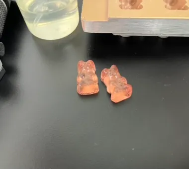 Two peach-colored bear-shaped Vitamin A gummies representing a fat-soluble formula developed with combined emulsifiers for uniform dispersion and consistent batch content.